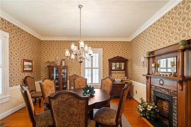 dining room featuring wallpapered walls, a brick fireplace, a wainscoted wall, and wood finished floors