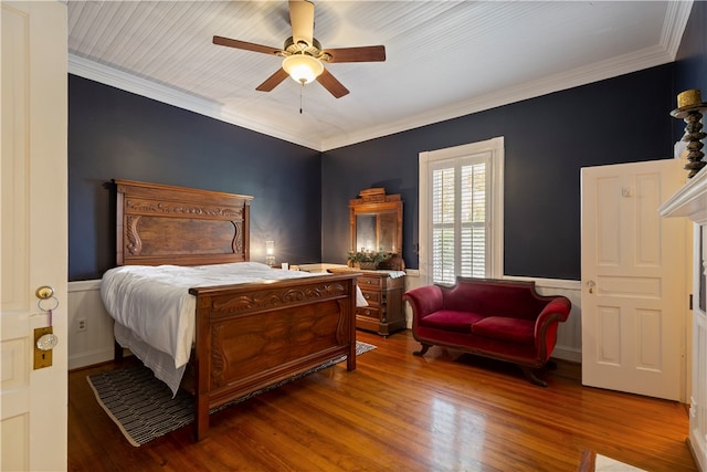 bedroom with a ceiling fan, a wainscoted wall, crown molding, and wood finished floors