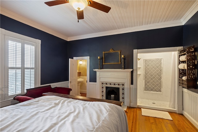 bedroom with crown molding, multiple windows, wood finished floors, and wainscoting