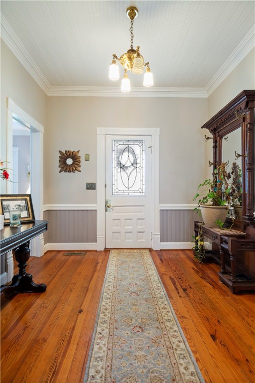 foyer with ornamental molding, wood-type flooring, a wainscoted wall, and a notable chandelier