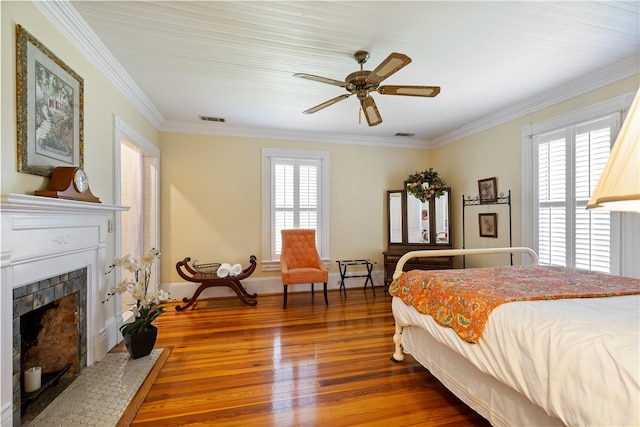 bedroom featuring a fireplace, wood finished floors, visible vents, baseboards, and ornamental molding