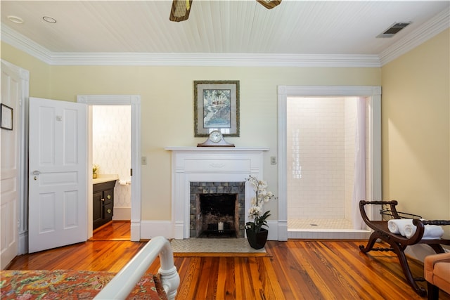 living room with ornamental molding, wood-type flooring, visible vents, and a fireplace