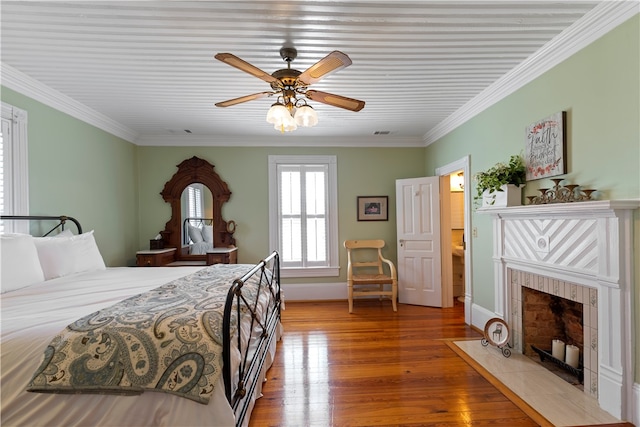 bedroom with a fireplace, wood finished floors, visible vents, and crown molding