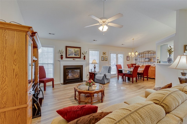 living room with ceiling fan with notable chandelier, light hardwood / wood-style floors, and vaulted ceiling