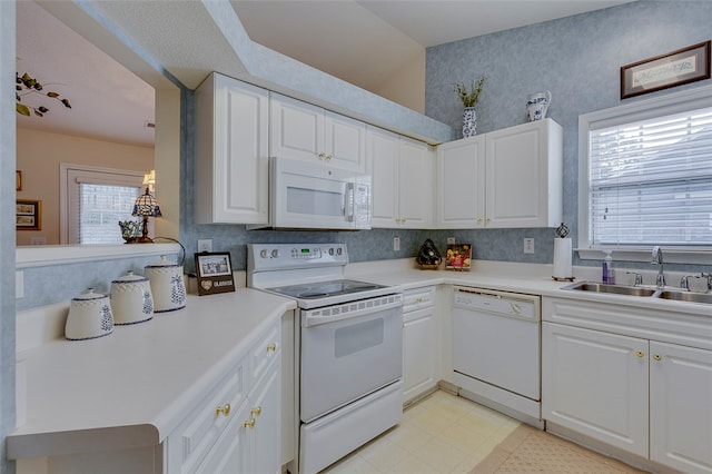 kitchen featuring kitchen peninsula, sink, white appliances, and white cabinetry