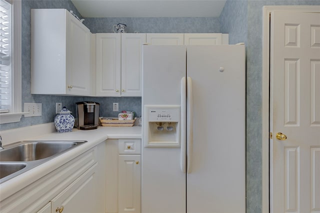 kitchen featuring white refrigerator with ice dispenser, sink, and white cabinets