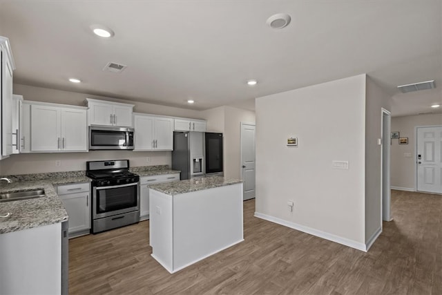 kitchen featuring appliances with stainless steel finishes, white cabinetry, light wood-type flooring, sink, and a center island