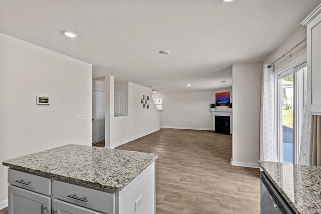 kitchen with a center island, dishwasher, light stone counters, and light wood-type flooring