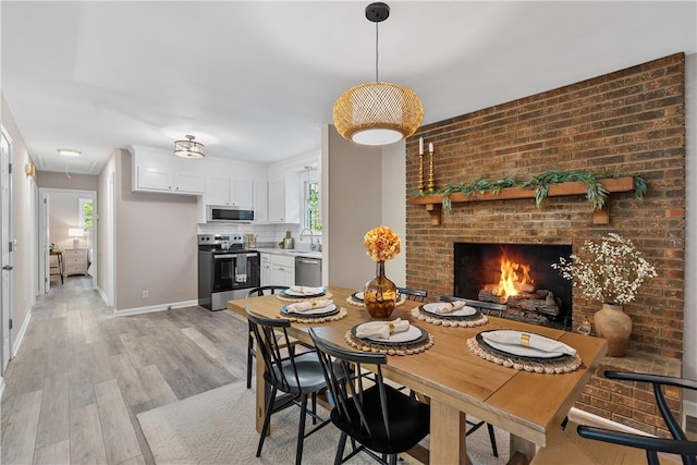 dining space featuring a fireplace, light wood-type flooring, brick wall, and sink