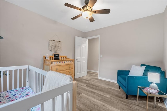 bedroom with light wood-type flooring, a nursery area, and ceiling fan