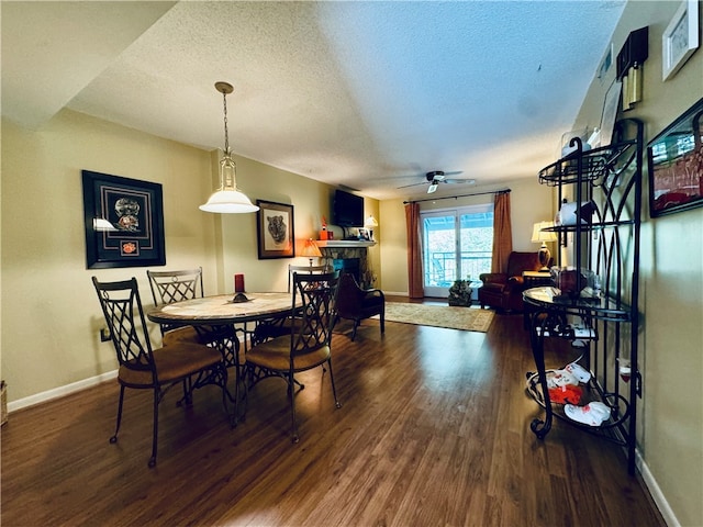 dining space with a stone fireplace, a textured ceiling, ceiling fan, and dark hardwood / wood-style flooring