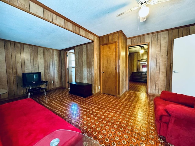 living room with wooden walls, a textured ceiling, and ceiling fan