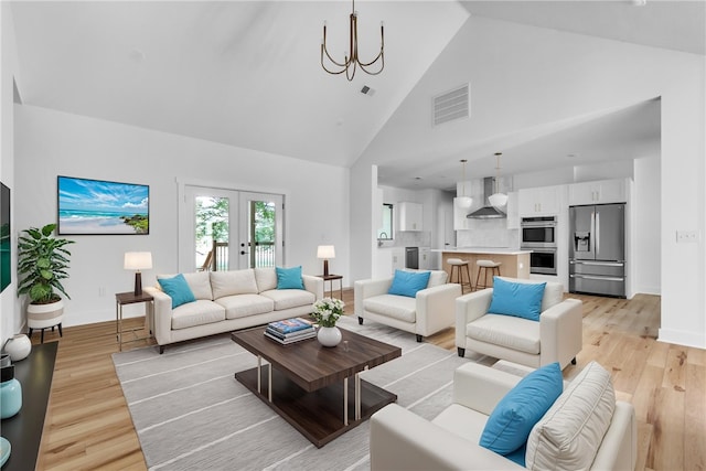 living room with light hardwood / wood-style flooring, french doors, high vaulted ceiling, and a notable chandelier