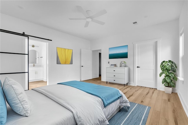 bedroom featuring a barn door, ceiling fan, ensuite bath, and light wood-type flooring