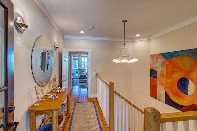 corridor featuring wood-type flooring, ornamental molding, and a chandelier