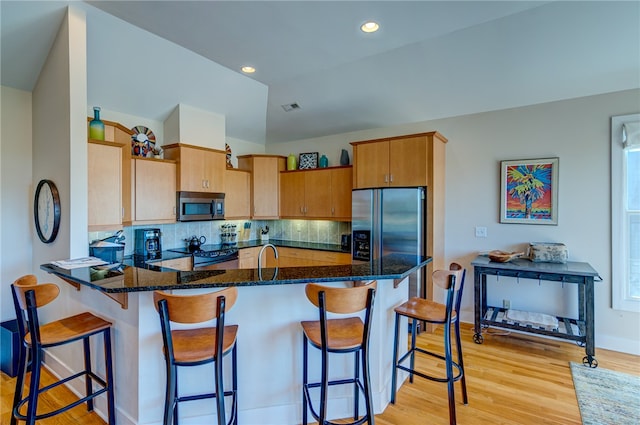 kitchen with kitchen peninsula, tasteful backsplash, appliances with stainless steel finishes, dark stone counters, and light hardwood / wood-style floors