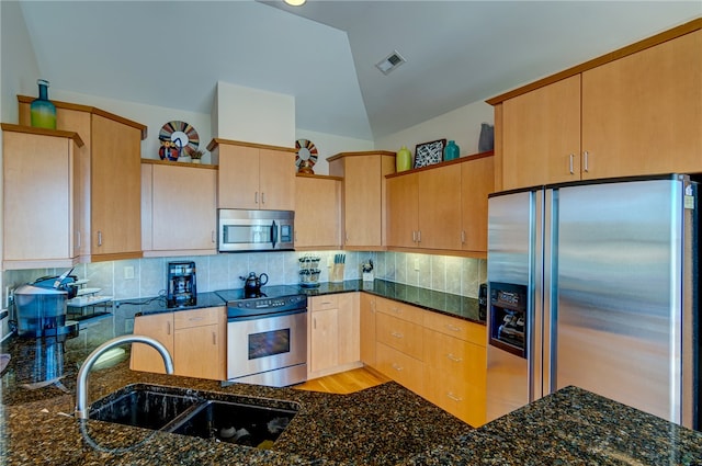 kitchen with sink, appliances with stainless steel finishes, vaulted ceiling, and dark stone counters