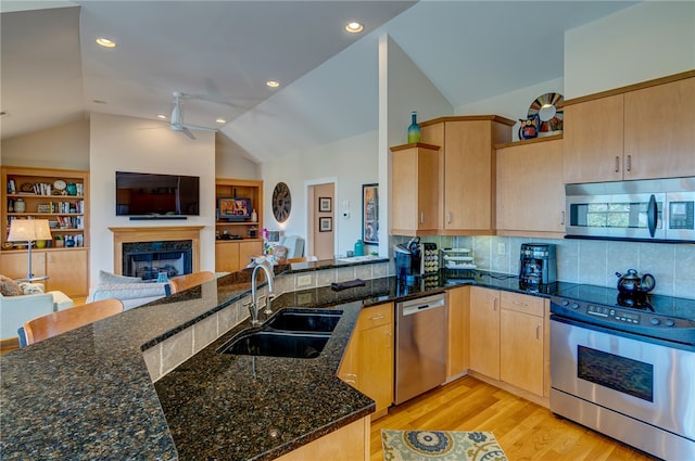 kitchen featuring lofted ceiling, kitchen peninsula, appliances with stainless steel finishes, dark stone counters, and sink