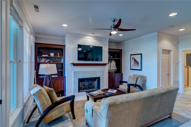 living room featuring a tiled fireplace, crown molding, light tile patterned floors, and ceiling fan