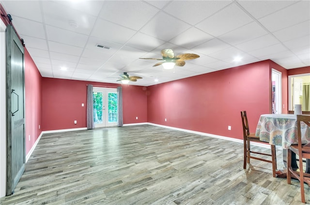 spare room with a barn door, ceiling fan, a drop ceiling, and wood-type flooring