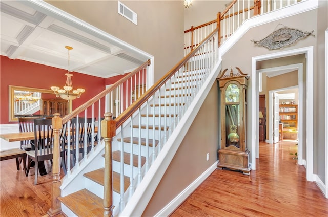 stairway with beam ceiling, hardwood / wood-style flooring, a notable chandelier, and coffered ceiling