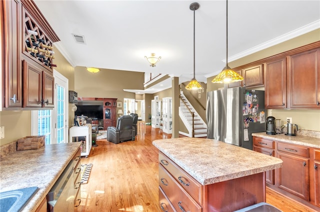 kitchen with hanging light fixtures, a kitchen island, ornamental molding, appliances with stainless steel finishes, and light hardwood / wood-style floors