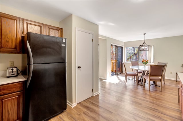 kitchen with an inviting chandelier, pendant lighting, light hardwood / wood-style floors, and black fridge