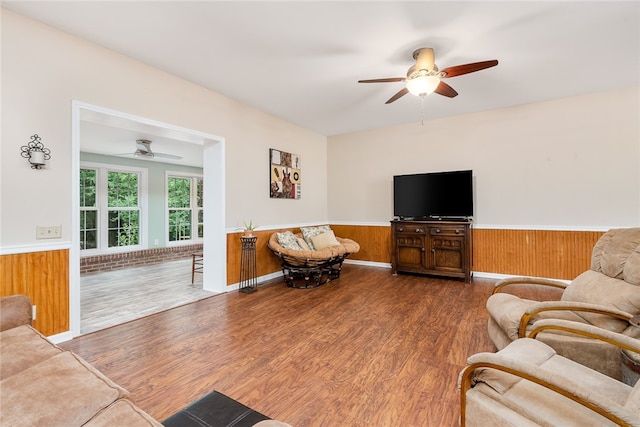 living room featuring hardwood / wood-style flooring, ceiling fan, and wooden walls