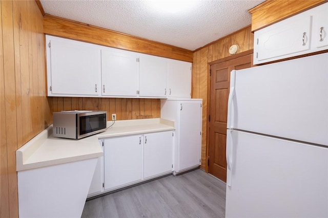 kitchen with light wood-type flooring, wood walls, white refrigerator, a textured ceiling, and white cabinets