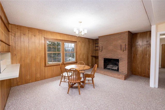 carpeted dining room with a brick fireplace, an inviting chandelier, wood walls, and a textured ceiling