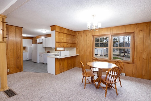 dining area with an inviting chandelier, a textured ceiling, wood walls, and light colored carpet