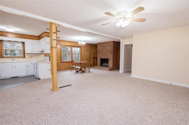 unfurnished living room with beam ceiling, wood walls, ceiling fan with notable chandelier, sink, and light colored carpet