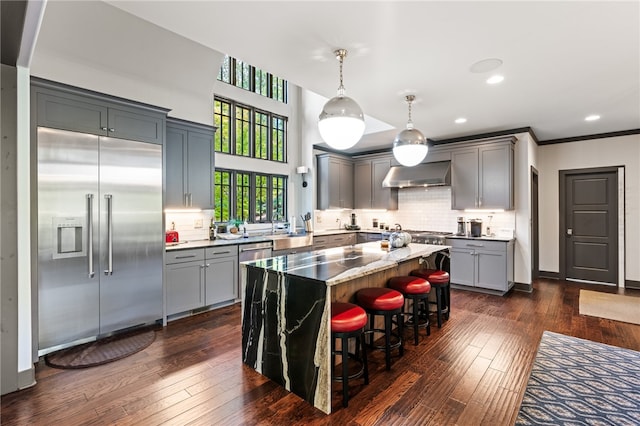 kitchen featuring a center island, appliances with stainless steel finishes, wall chimney range hood, and dark hardwood / wood-style floors