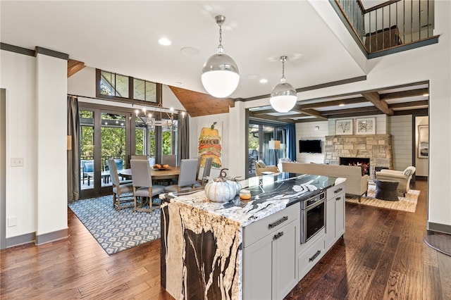 kitchen featuring stainless steel oven, white cabinetry, pendant lighting, dark wood-type flooring, and light stone counters