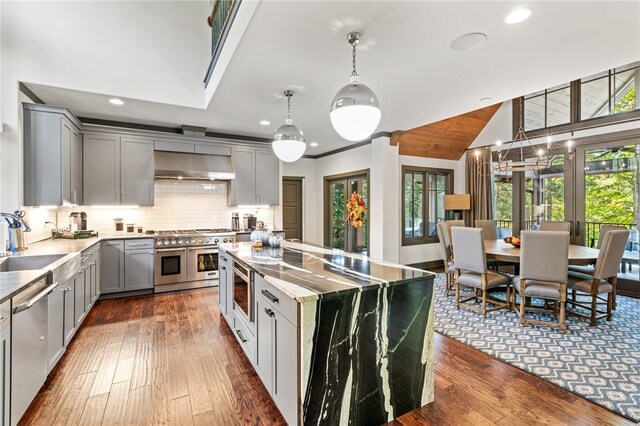 kitchen with gray cabinets, wall chimney exhaust hood, stainless steel appliances, and a wealth of natural light