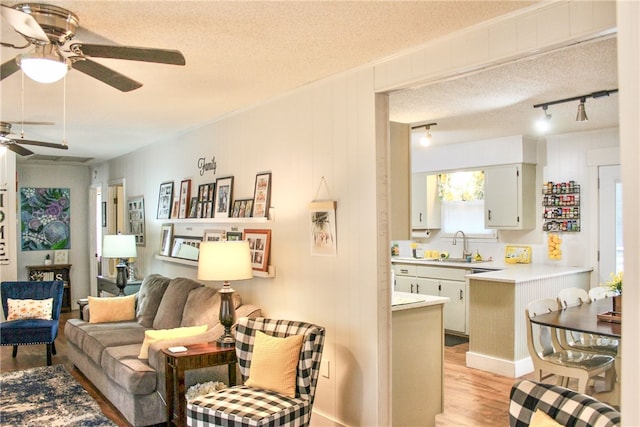 living room featuring track lighting, light hardwood / wood-style flooring, a textured ceiling, and ceiling fan