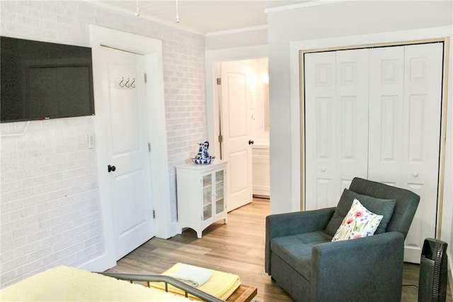 sitting room featuring brick wall, ornamental molding, and wood-type flooring