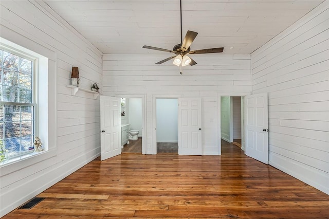 unfurnished bedroom with ensuite bath, ceiling fan, wood walls, a towering ceiling, and hardwood / wood-style flooring