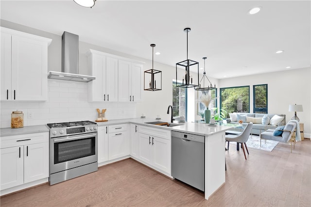 kitchen with white cabinetry, sink, pendant lighting, wall chimney exhaust hood, and stainless steel appliances