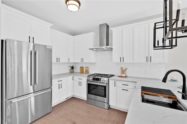 kitchen with wall chimney range hood, appliances with stainless steel finishes, sink, white cabinetry, and light stone counters