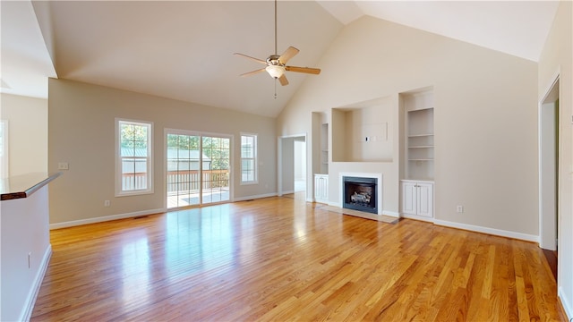 unfurnished living room featuring high vaulted ceiling, built in shelves, light hardwood / wood-style floors, and ceiling fan