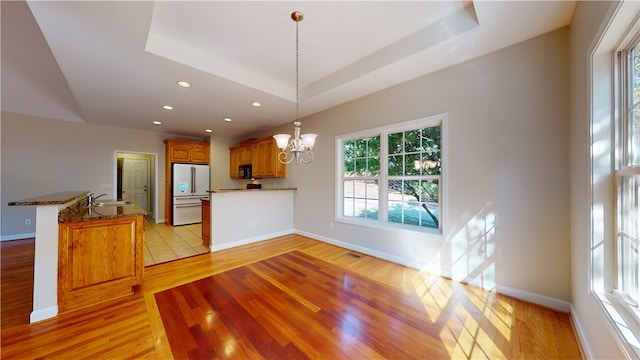 living room with an inviting chandelier, a tray ceiling, sink, and light wood-type flooring