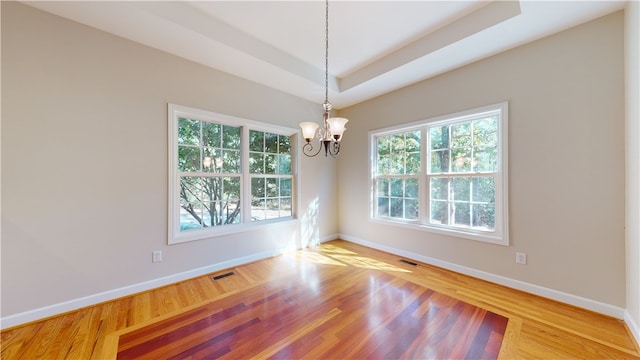 unfurnished room with a raised ceiling, a chandelier, and light hardwood / wood-style flooring