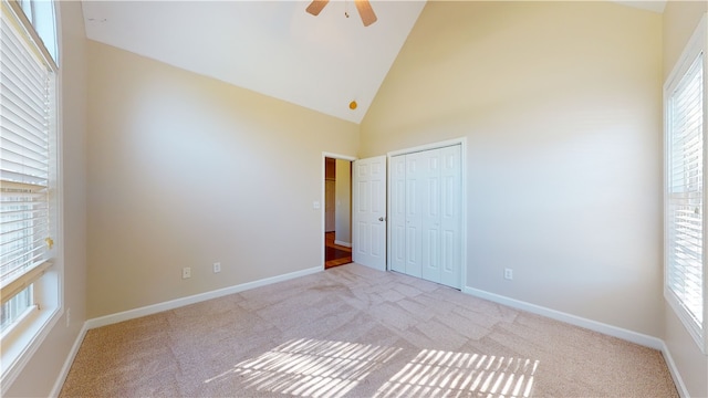 unfurnished bedroom with ceiling fan, light colored carpet, high vaulted ceiling, and a closet