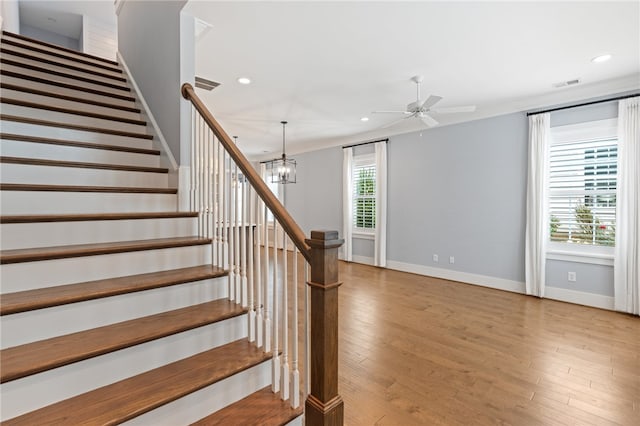 staircase with crown molding, hardwood / wood-style flooring, and ceiling fan with notable chandelier