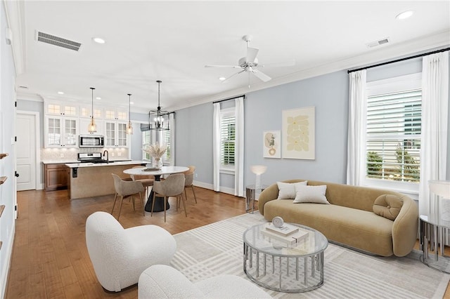 living area with ornamental molding, recessed lighting, wood finished floors, and visible vents