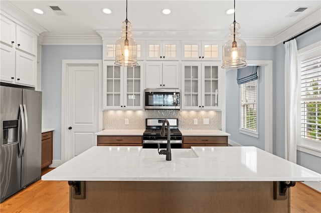 kitchen featuring appliances with stainless steel finishes, white cabinetry, a kitchen island with sink, and decorative light fixtures