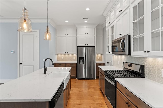 kitchen with appliances with stainless steel finishes, a sink, light wood finished floors, white cabinetry, and decorative light fixtures