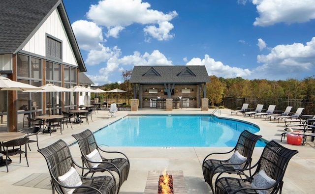 pool with exterior bar, fence, an outdoor structure, an outdoor fire pit, and a patio