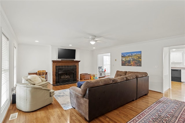 living room featuring a tiled fireplace, light hardwood / wood-style floors, and crown molding